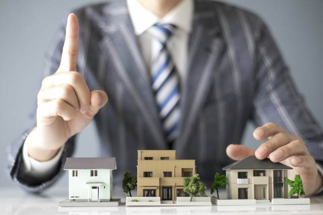 家の模型を見せ人差し指を立てる男性