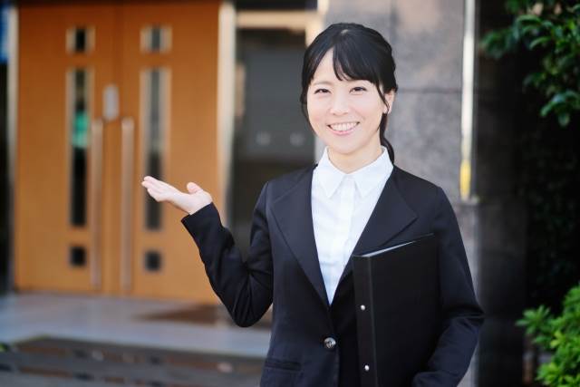 右手を広げ家を紹介する女性
